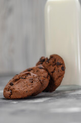 cookies with pieces of chocolate on a table next to a bottle of milk
