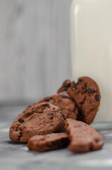 cookies with pieces of chocolate on a table next to a bottle of milk