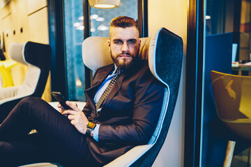 Portrait of confident businessman dressed in formal wear looking at camera while sitting in comfortable chair in office interior. Confident in future corporate entrepreneur feeling thoughtful