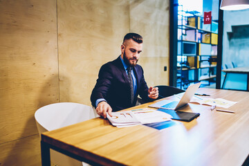 Prosperous intelligent businessman dressed in stylish suit checking documents and online database on modern laptop device using wireless internet.Successful proud ceo working at digital netbook