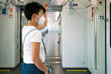 Asian female wearing mask hold hand rail and keep distancing in subway during coronavirus or covid-19 virus outbreak a new normal concept