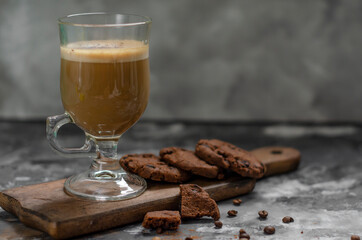 a cookie with pieces of chocolate tied with a string lies on a wooden board and next to a cup of latte