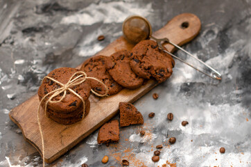 a cookie with pieces of chocolate tied with a string lies on a wooden board and next to a cup of latte