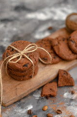 a cookie with pieces of chocolate tied with a string lies on a wooden board and next to a cup of latte