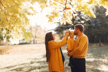 Family in a autumn park. Woman in a yellow sweater. Cute little girl with parents