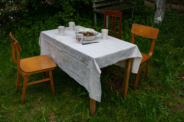 Outside table with mugs and meat and old chairs