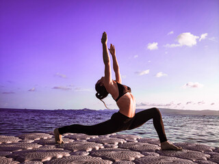 Fototapeta na wymiar a sporty girl of European appearance does yoga in the fresh air on a pier near the sea