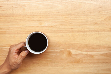 Hand holding a cup of coffee on wooden table. Top view and copy space
