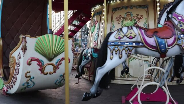 Close up interior view of a moving carousel with colorful retro vintage wooden seats and horses moving up and down without people. The atmosphere of the holiday and amusement park