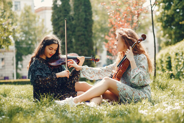 Girls in a summer park. Two ladies with a violin. Friends sitting on a grass