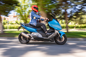 Moto tipo scooter circulando por una calle con arboles y día soleado