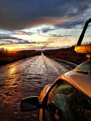 Traveling by car on a dirt country road to sunset after rain