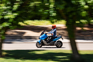 Fototapeta na wymiar Moto tipo scooter circulando por una calle con arboles y día soleado