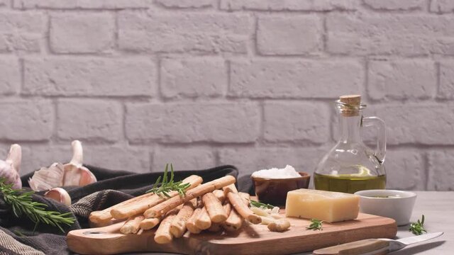 Fresh baked homemade grissini bread sticks in vintage metal grid box with olive oil and rosemary herbs over kitchen counter top.