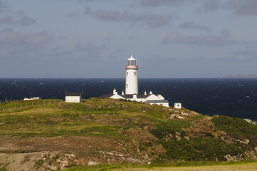 Magnifique phare blanc posé sur des falaises rocheuses et verdoyantes au bord de la mer bleu indigo de l'Irlande du nord.
