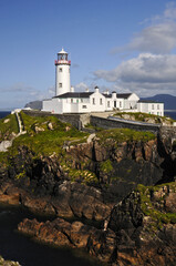Fototapeta na wymiar Magnifique phare blanc posé sur des falaises rocheuses et verdoyantes au bord de la mer bleu indigo de l'Irlande du nord.