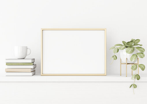 Poster mockup with horizontal gold metal frame on the table with green plant in pot, books, cup and trendy interior decoration on empty white wall background. A4, A3 size. 3D rendering, illustration.