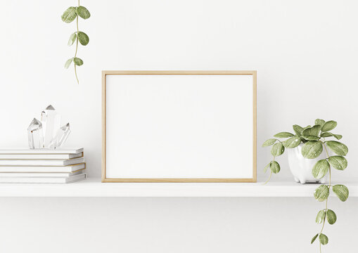 Interior poster mockup with horizontal wooden frame on the shelf with green plant in pot, books, crystals and trendy decoration on empty white wall background. A4, A3 size. 3D rendering, illustration.
