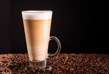 Coffee latte with frothy milk in tall glass, on coffee beans.