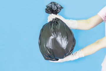 White latex gloves on a woman's hand,Carrying a black garbage bag outstretched isolated on blue background