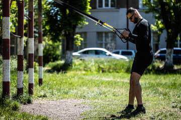 young muscular sportsman training with trx resistance bands in the park