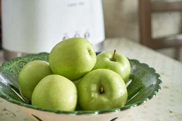 Several green apples in a beautiful green dish on the kitchen table. Green apples shot close.