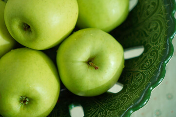 Several green apples in a beautiful green dish on the kitchen table. Green apples shot close.