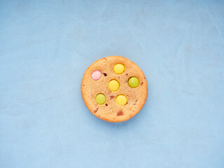 top view of a single cookie with colored candy embedded on top of a blue surface