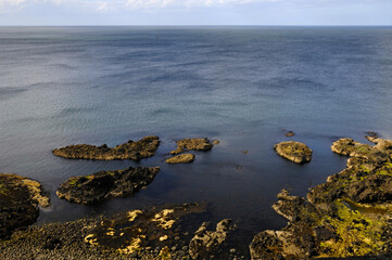 Vue panoramique sur l'horizon, les rochers et la mer bleue indigo depuis la côte verdoyante du...