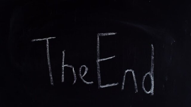 A man's hand in a shirt writes the end word end. The inscription end on the blackboard. The hand writes the end in chalk on the blackboard