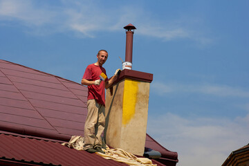 man with a brush on the roof,man roofer on the roof stands with a brush to paint the chimney