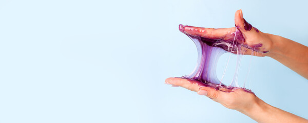 Young girl hands with sticky purple slime on blue background, liquid wax for depilation, conceptual flyer banner with copy space, antistress relax, modern kids hobby oddly satisfying semi surreal asmr - 358120353