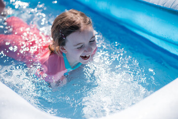 Fototapeta na wymiar Little girl has fun splashing in paddling pool in summer