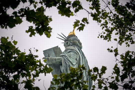 Low angle shot of the amazing Statue of Liberty visible through tree branches - Powered by Adobe