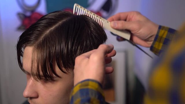 Close-up of master cut hair of young man using scissors with comb