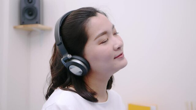 Asian teenage woman using the bluetooth headphone for listening to streaming music so lovely lie in bed. slow motion in a studio shot.