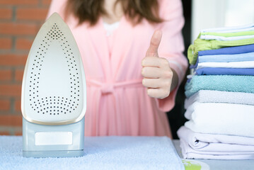 Woman is ironing a clothes and is showing a thumbs up gesture close up.