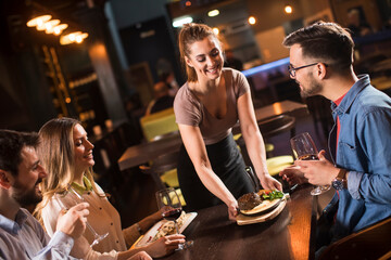 Waiter woman serving group of friends with food in the restaurant