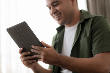 Handsome man checking social media with tablet computer at the the bedroom, living room. Communication and technology concept