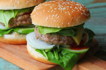 Homemade hamburger with beef, onion,cucumber, lettuce, cheese, spinach and spices. Fresh burger closeup on wooden cutting board
