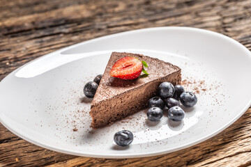 Triangular slice of a chocolate mousse cake with blueberries and strawberry