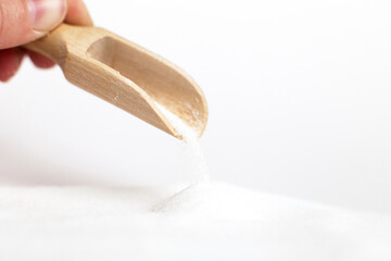 hand with a wooden spoon of salt grain on white background