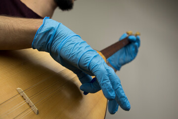 A man is playing a traditional string instrument called as 'baglama' in Turkish. He wears blue surgical gloves as a precation because of the covid-19 pandemic outbreak. New normal concept.