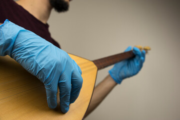 A man is playing a traditional string instrument called as 'baglama' in Turkish. He wears blue surgical gloves as a precation because of the covid-19 pandemic outbreak. New normal concept.