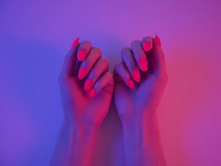 Woman hands with beautiful bright orange manicure in neon light.