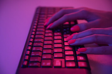 Woman with orange manicure working on wireless keyboard in neon light.