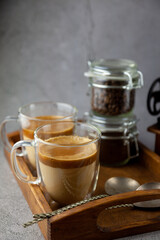 Iced Dalgona coffee drink on wooden tray background. Instant coffee or espresso powder whipped with sugar and hot water. Coffee with milk latte, cappuccino. Two glass cups with double walls. Breakfast