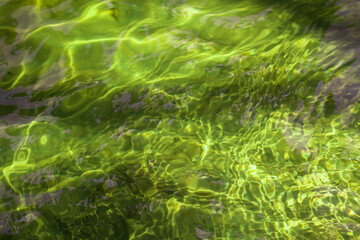 Emerald color. Water ripples. The radiance of the sun in the water. Pattern of water on a sand bottom background. Sun rays in the river. A refreshing screensaver. Water theme. Bright shining waves.