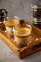 Iced Dalgona coffee drink on wooden tray background. Instant coffee or espresso powder whipped with sugar and hot water. Coffee with milk latte, cappuccino. Two glass cups with double walls. Breakfast