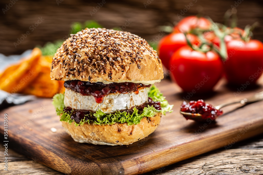 Wall mural Vegetarian burger with camembert and cranberry sauce on a rustic wooden board